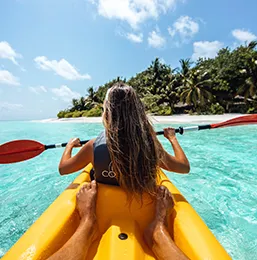 A couple canoeing in a blue ocean with a white sand beach background
